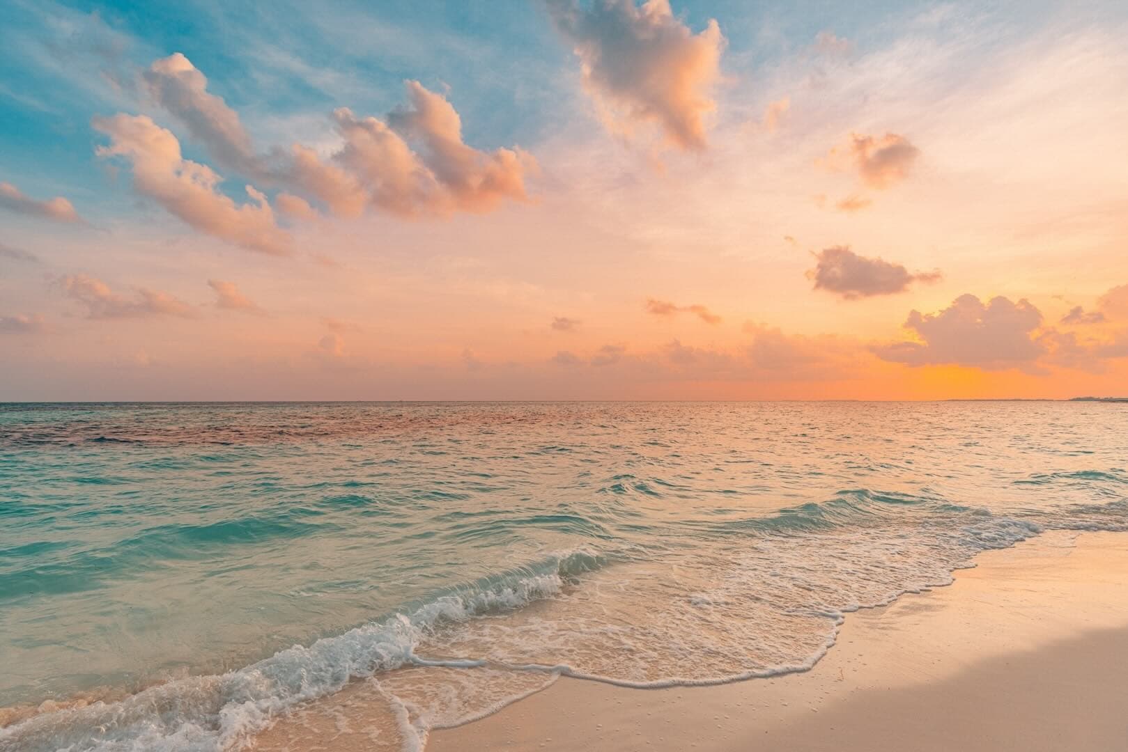 A calm sea and a beach, at sunset, with waves gently reaching the beach