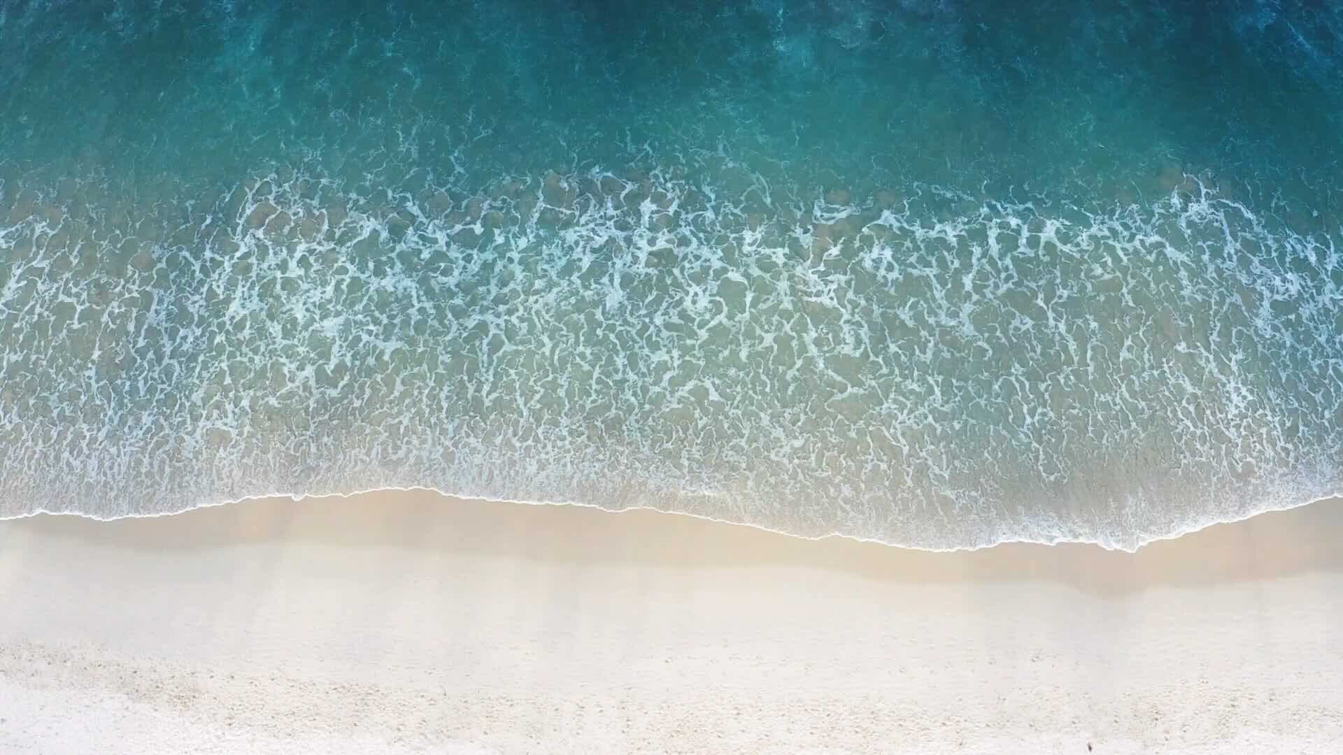 A view from above,  of a beach, with waves of a deep blue water gently crashing on the sand