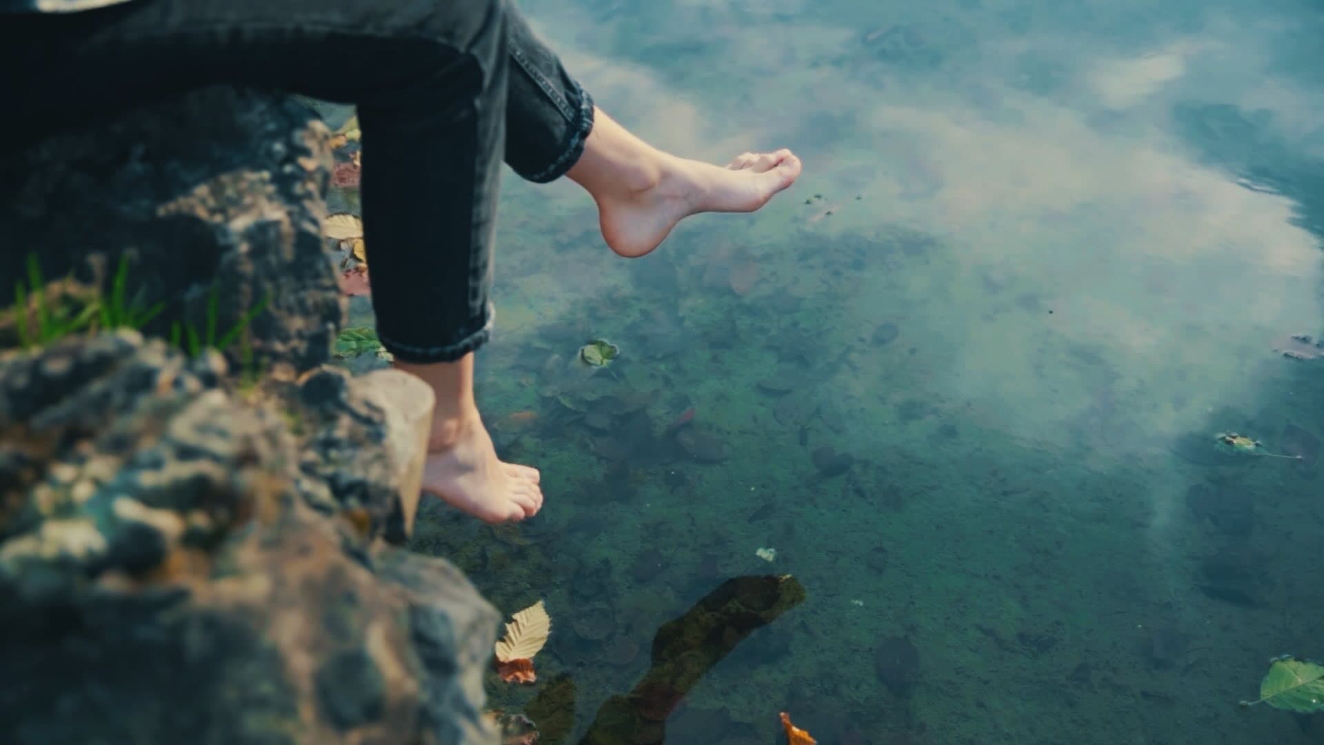 Les jambes d'une femme assise au bord d'un étang, balançant ses jambes d'avant en arrière au-dessus de l'eau