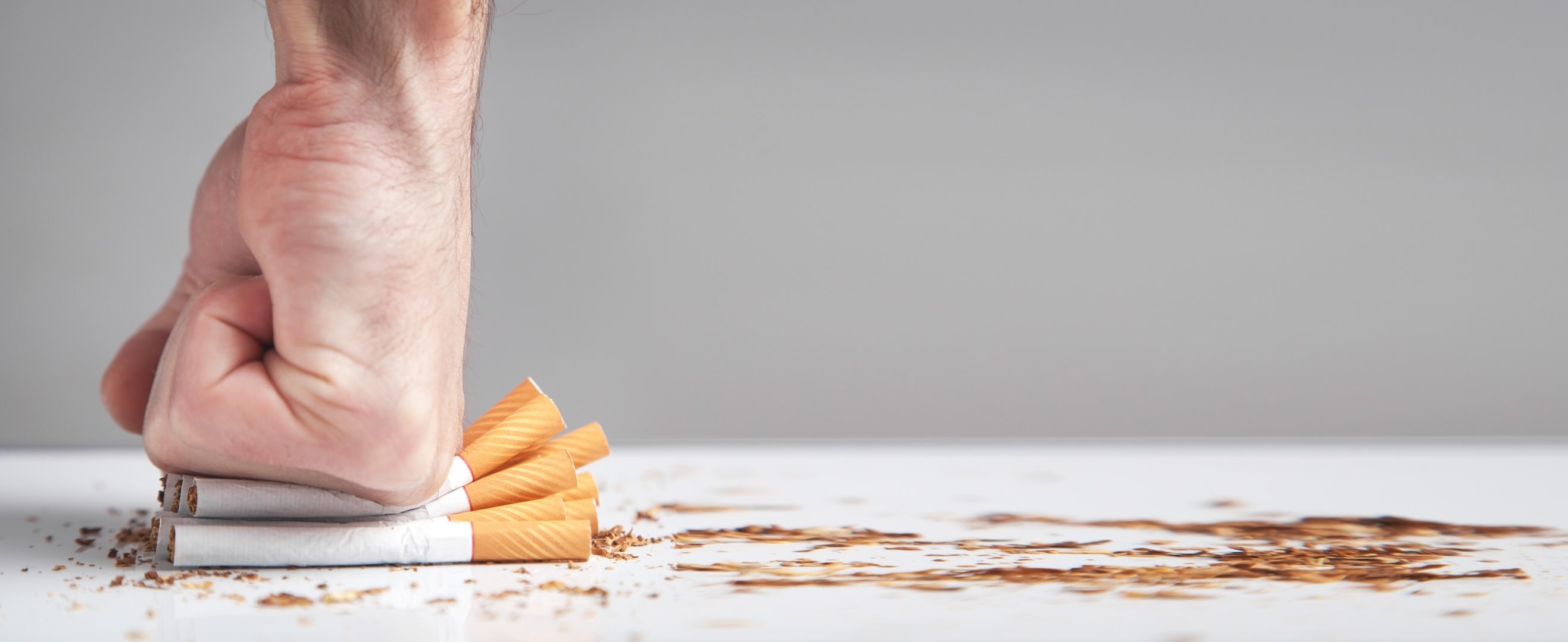 A white male's fist punching down on cigarettes, crushing them, with spills of tobacco around