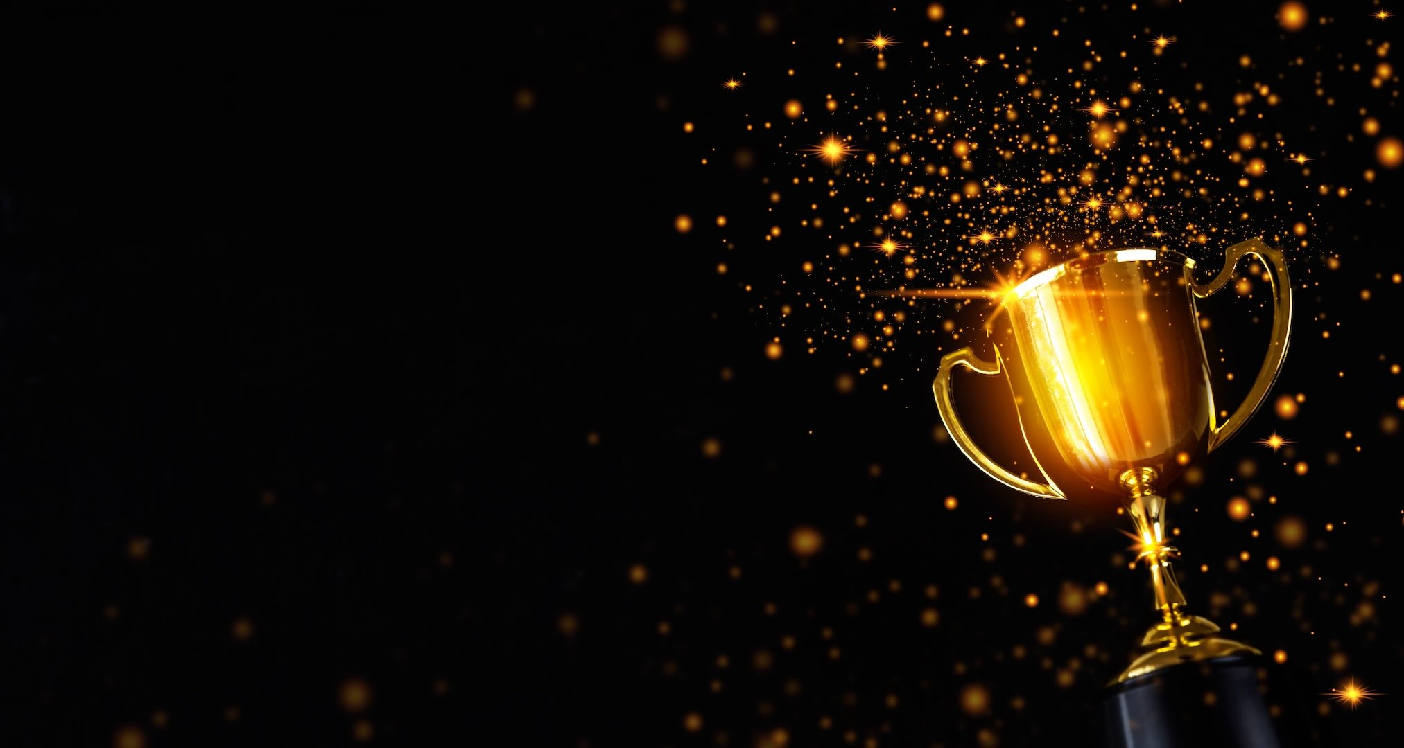 A shiny winning golden trophy, slightly tilting to the left, with golden sparkles around it