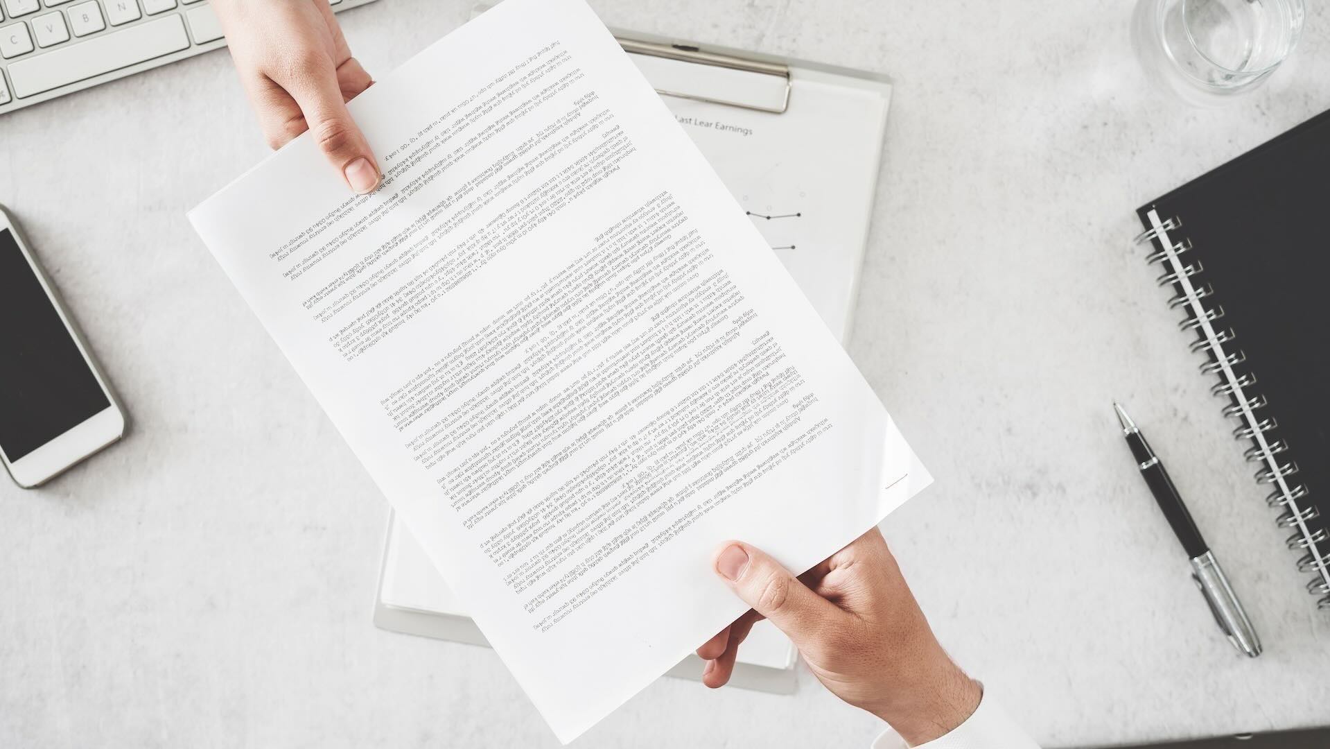2 hands coming from the top and bottom of the photo, passing a printed document to each other