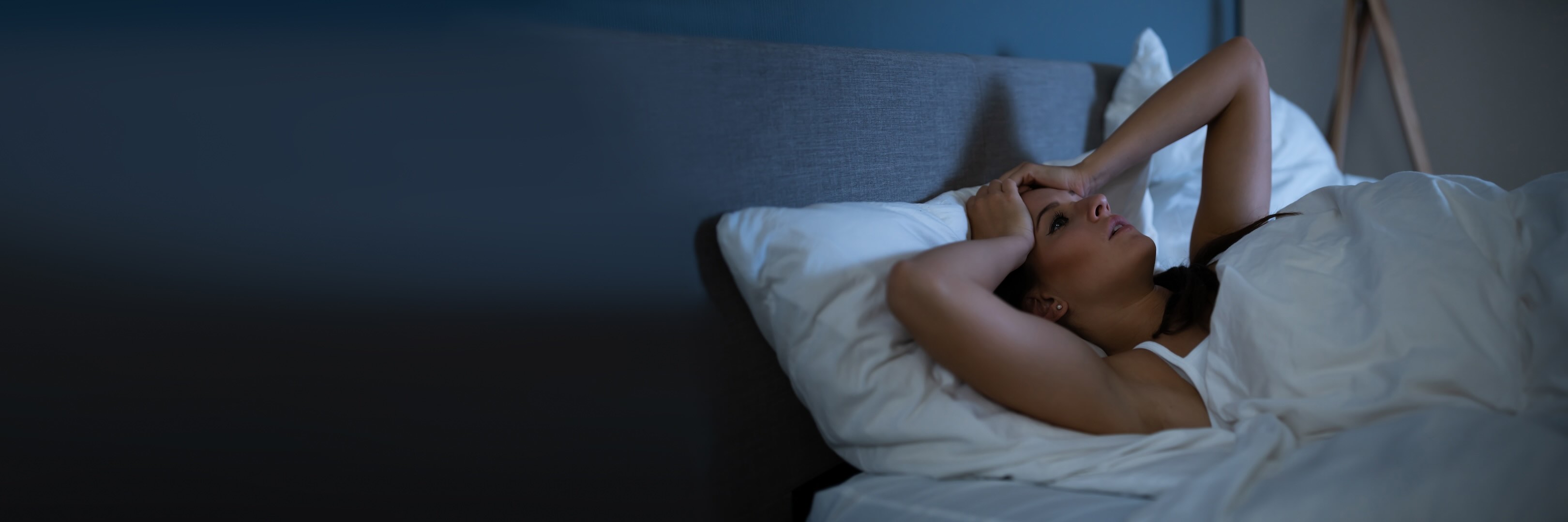 White female in bed, unable to find sleep, with her hands on her head, in apparent frustration