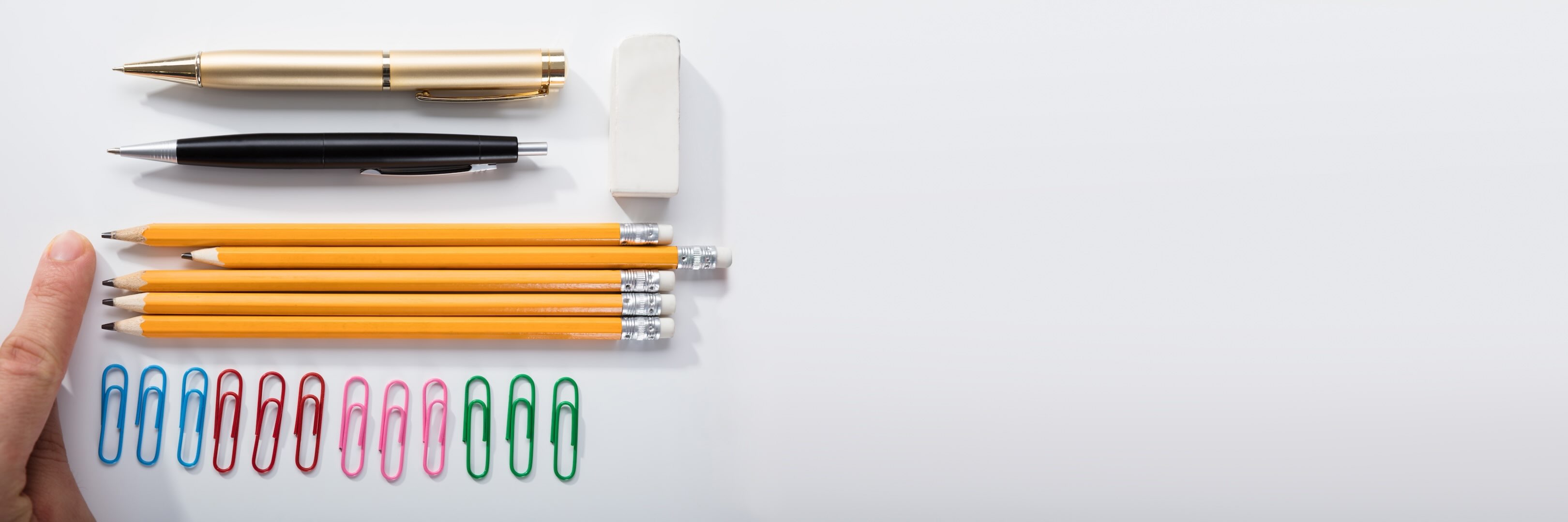 Various pens, an eraser, and paperclips, arranged carefully by color and types, except one paper pen